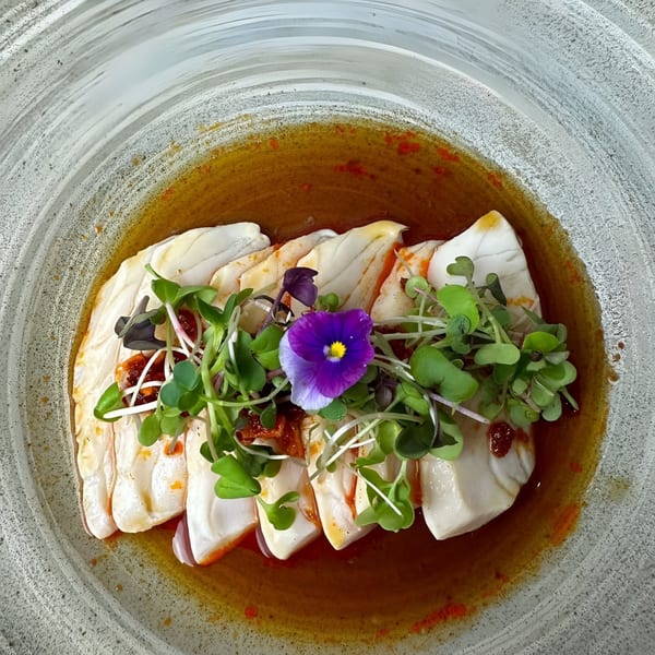 Top Sushi's white fish sashimi with microgreens, chili oil, and a purple edible flower.