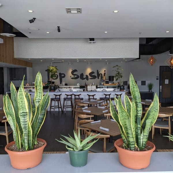 The interior of Top Sushi restaurant, featuring a sushi bar, dining tables, and potted plants.