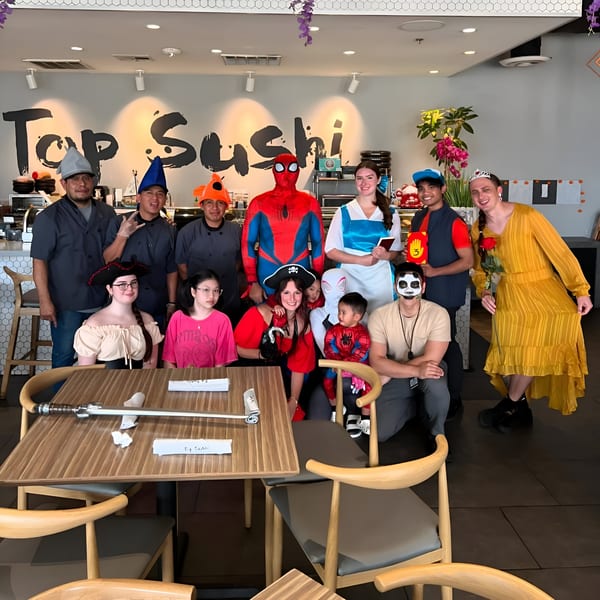 Top Sushi staff and guests in Halloween costumes pose together in the restaurant dining area.