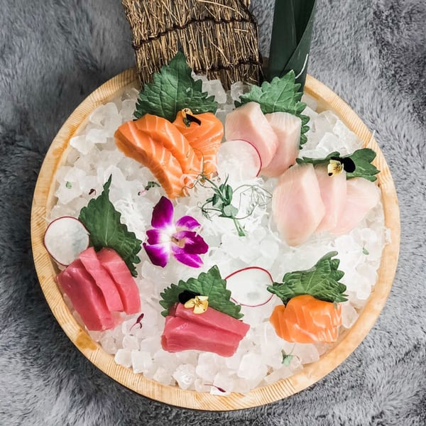 Top Sushi's sashimi platter with salmon, tuna, and white fish on ice, garnished with radish and orchids.