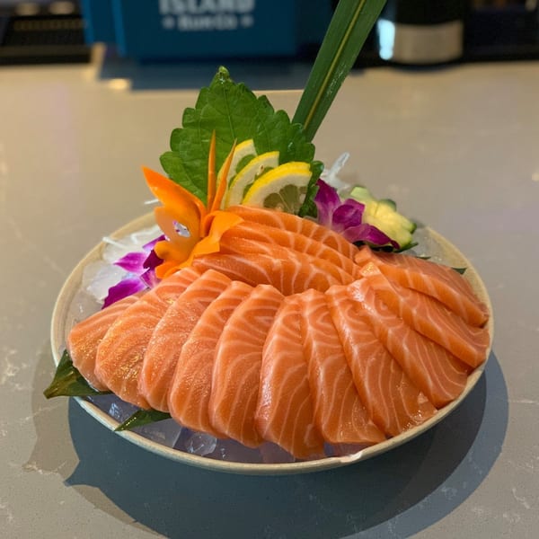 Platter of fresh salmon sashimi, garnished with lemon, cucumber, and a purple orchid.