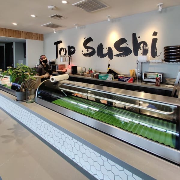 A Top Sushi employee behind the counter with a sushi display case in the foreground.